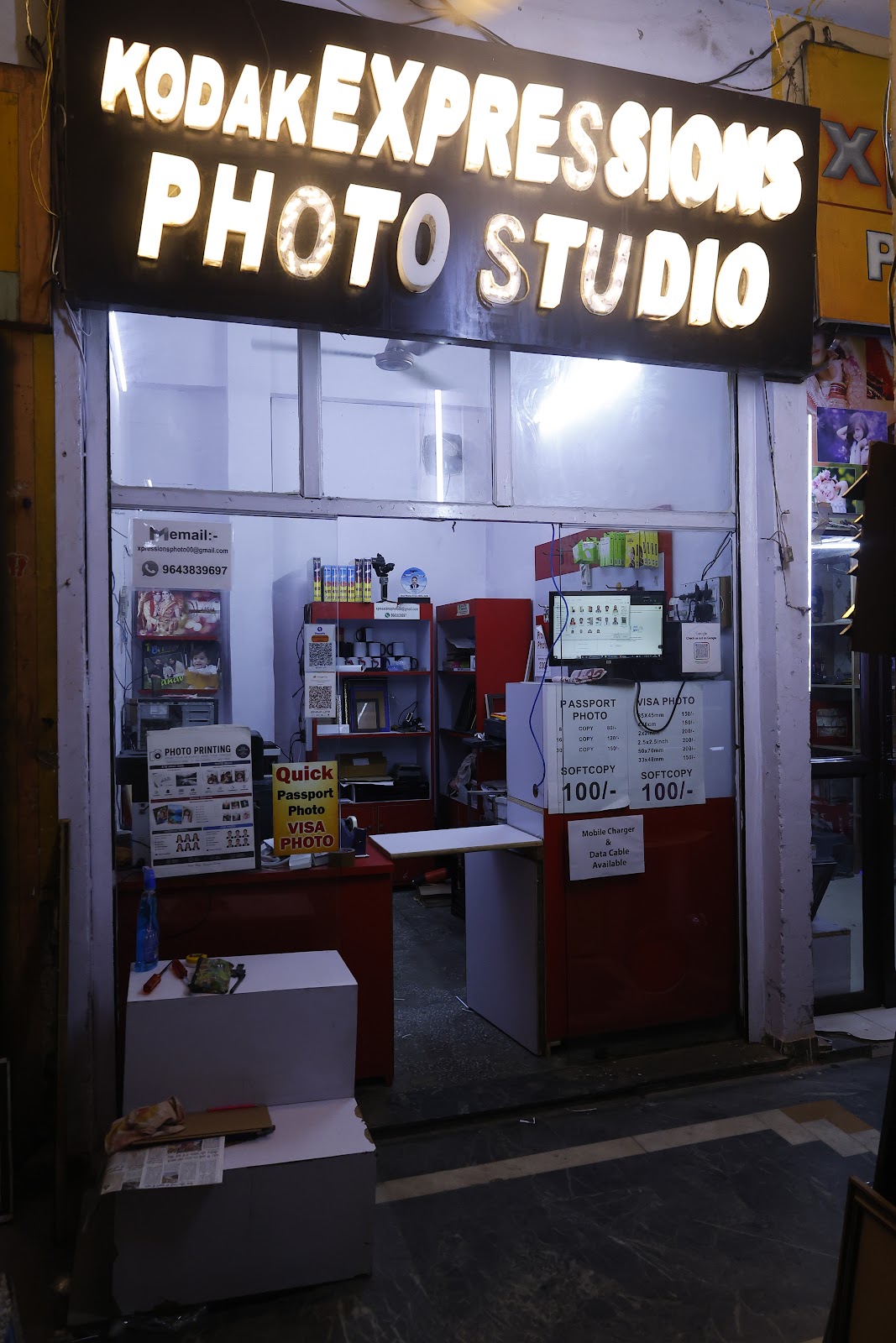 The studio counter at night, with passport and visa photo rate cards in the window